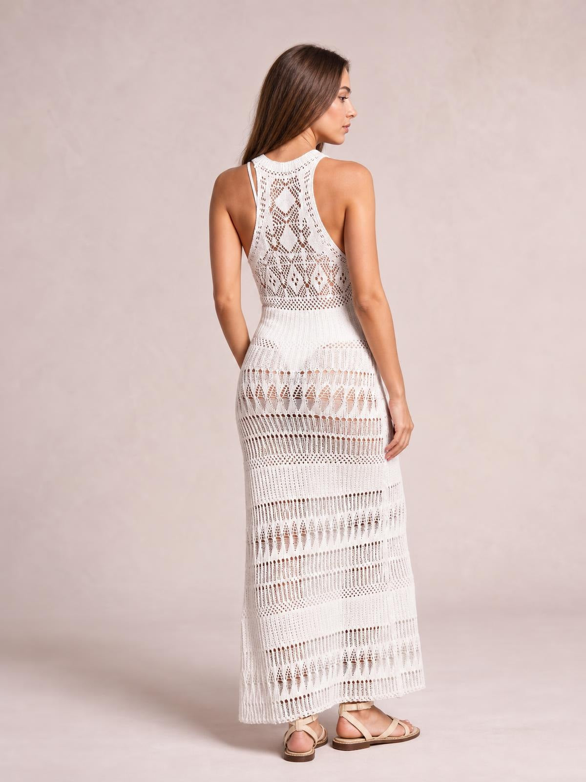 Model poses in a white crochet sleeveless split cover-up maxi dress with a fitted waist, openwork cutouts, and a long sheer silhouette.