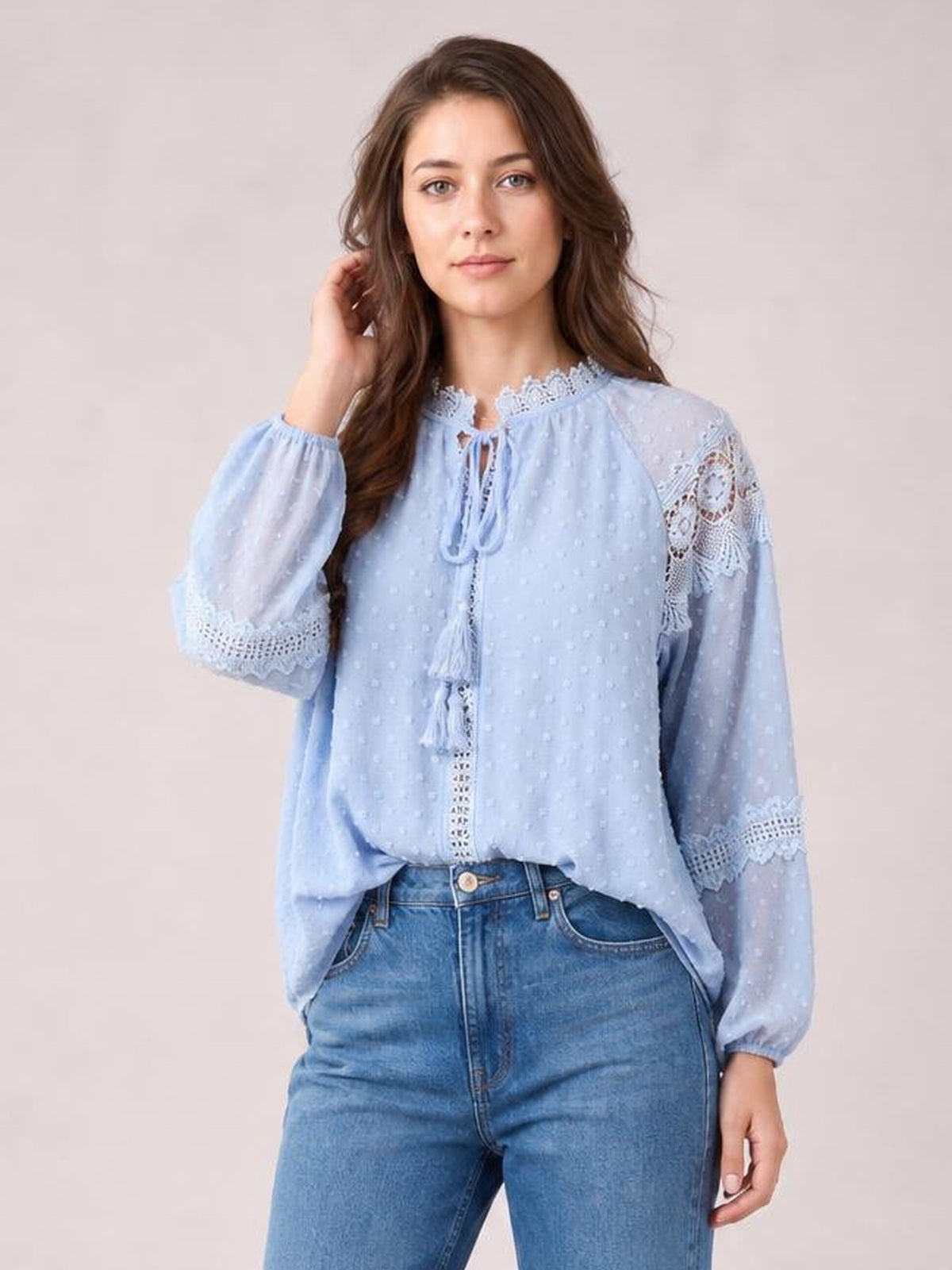 Model wears a light blue crochet tassel tie-neck blouse with long semi-sheer sleeves, lace trim, textured dots, and a relaxed silhouette.