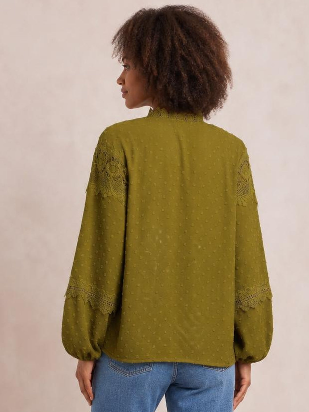 Model shown from behind wearing an olive green crochet blouse with long sleeves, textured fabric, lace sleeve panels, and a relaxed straight silhouette.