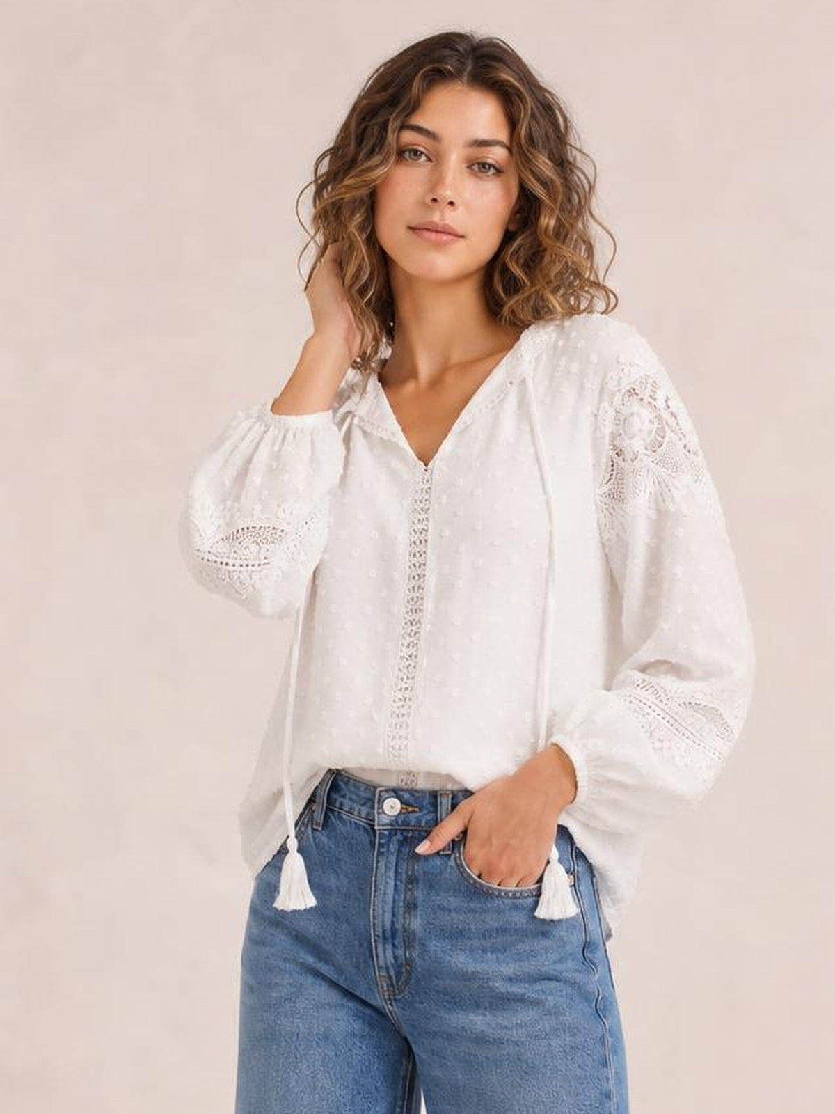 Model wears a white semi-sheer crochet tassel tie-neck long-sleeve blouse with a loose silhouette, textured fabric, and decorative sleeve trim.