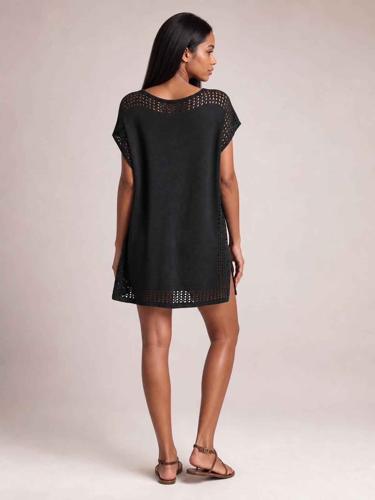 Model poses from the back in a black beach cover up dress with a loose silhouette, crochet trim, openwork cutouts, short sleeves, and side slits.