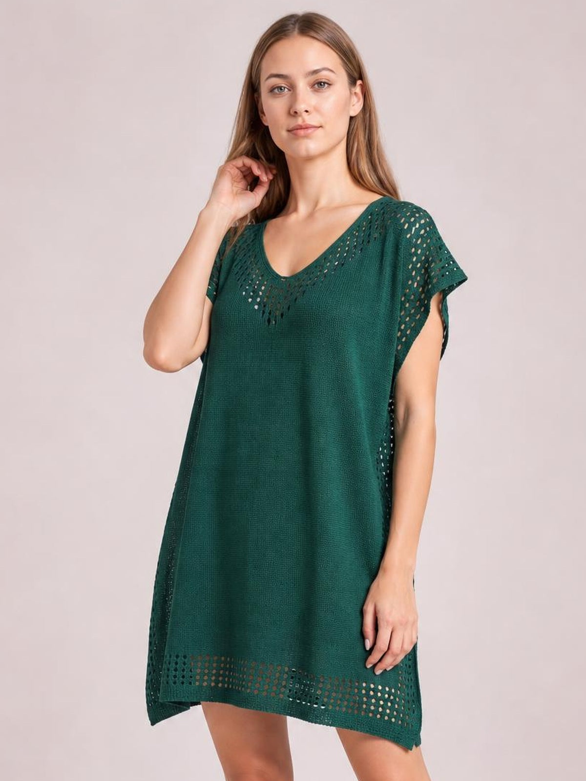 Model poses in a deep green beach cover-up dress with a loose silhouette, crochet-trim cutouts at the neckline, sleeves and hem, and side slits.