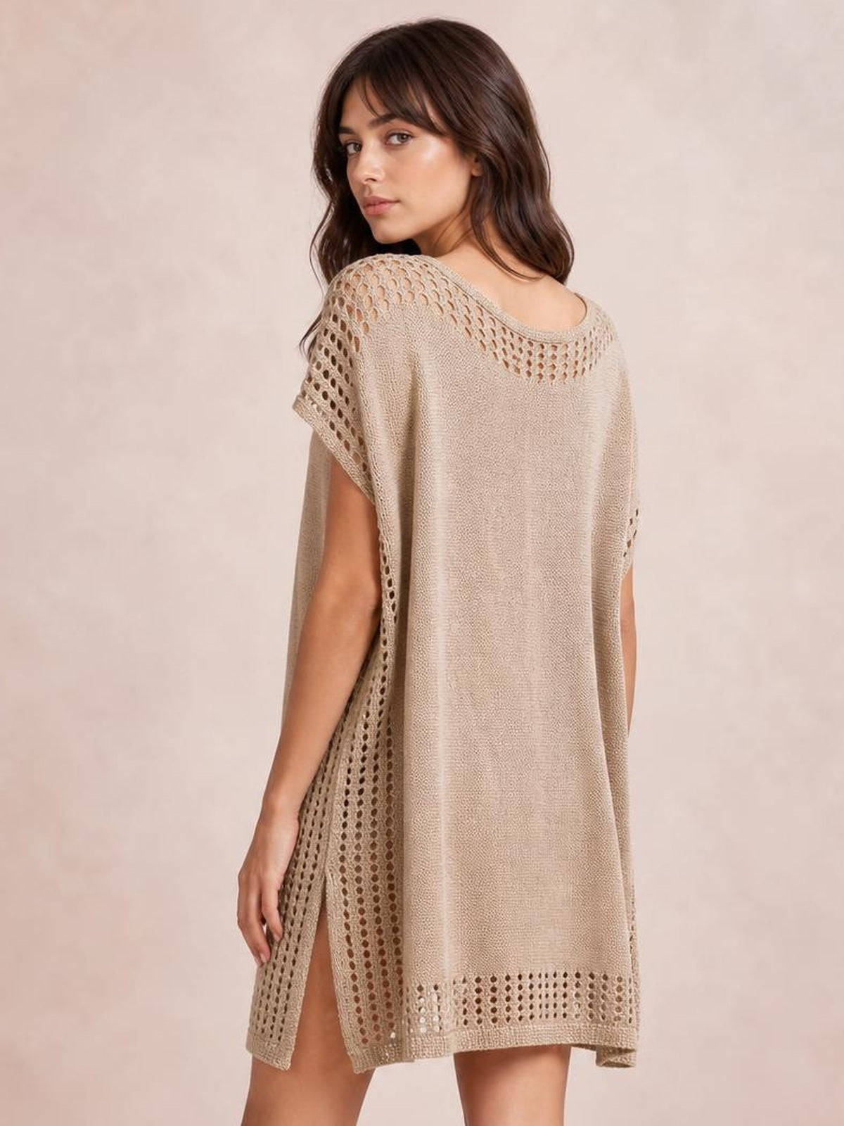 A model looks over her shoulder in a beige beach cover up dress with a loose silhouette, crochet trim, openwork cutouts, and side slits.