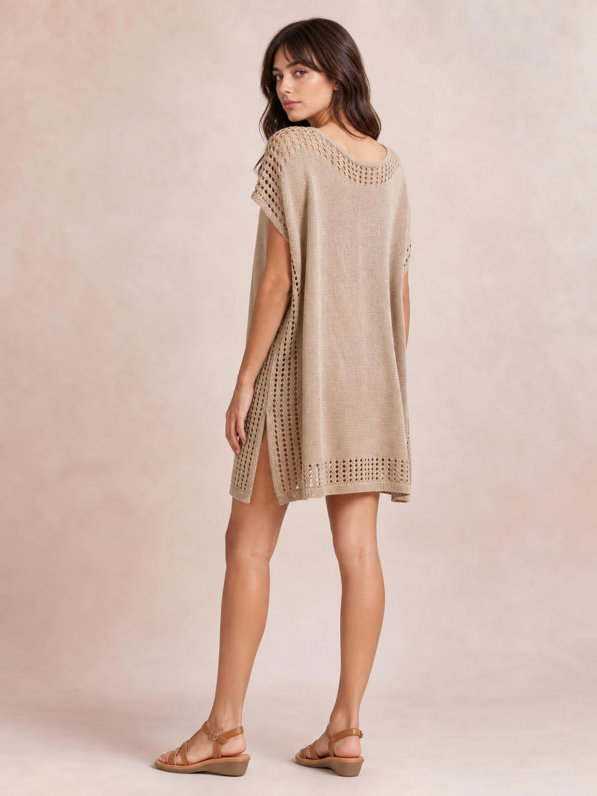 Model poses turned away in a beige crochet trim beach cover-up dress with a loose knee-length silhouette, openwork cutouts, and a side slit.
