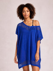 A model stands in a bright blue beach cover up dress with an off-shoulder neckline, relaxed tunic silhouette, and crochet-style openwork trim on the sleeves and hem.