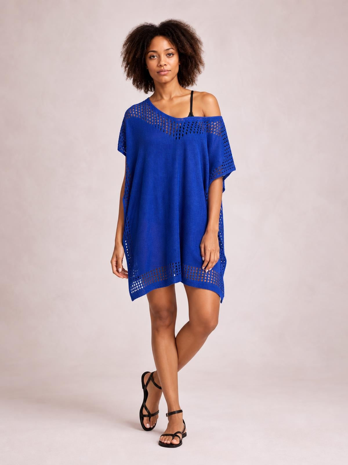 Model poses in a bright blue crochet-trim beach cover up dress with a relaxed tunic silhouette, off-shoulder neckline, cutout edging, and side slits.