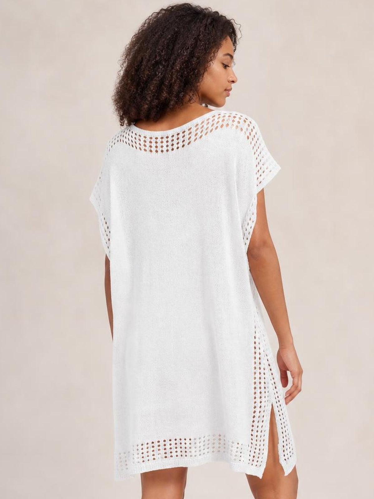 A model wears a white crochet trim beach cover up dress with a loose silhouette, openwork edging, short sleeves, and a high side slit.