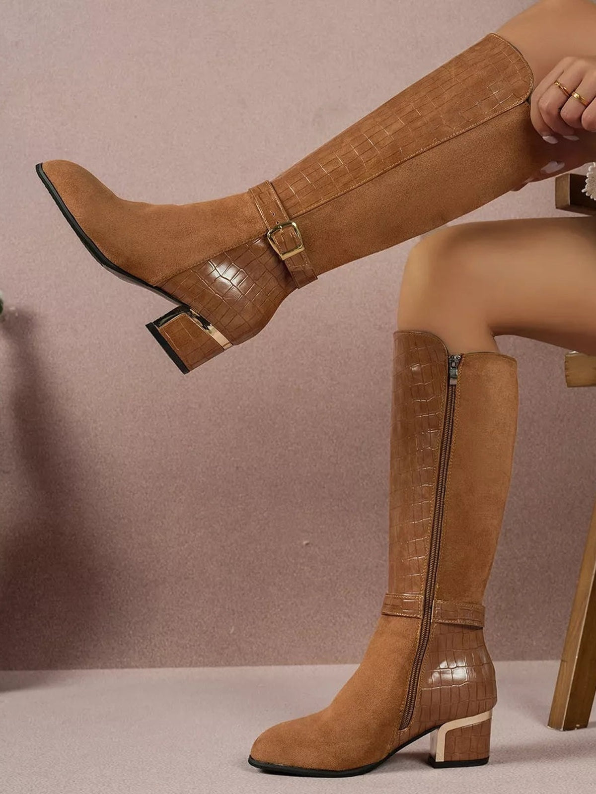 A model displays tan knee-high boots with crocodile-textured panels, suede-like shafts, side zippers, buckle straps, square toes, and low block heels.