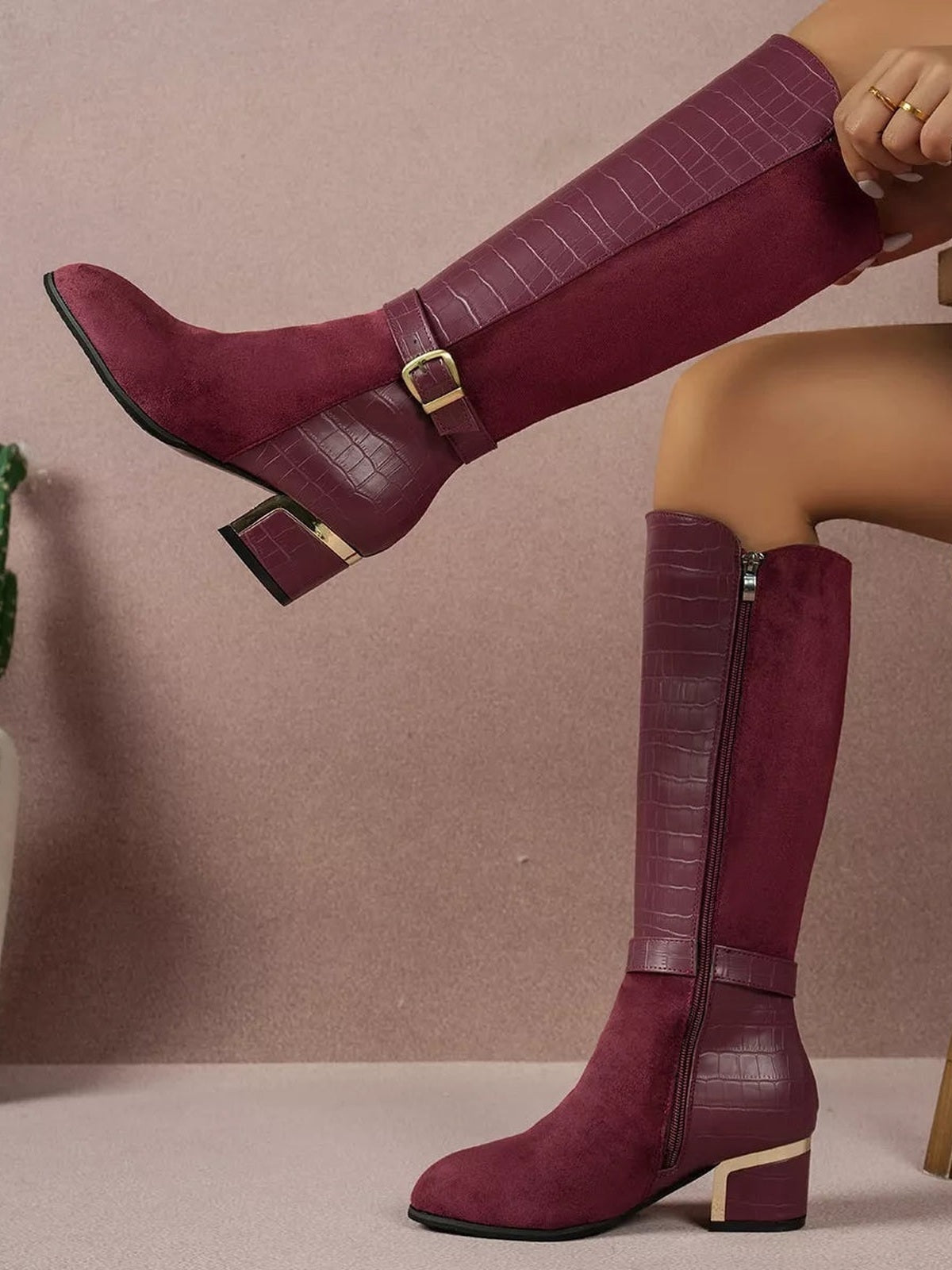 Burgundy knee-high boots feature suede-textured shafts, crocodile-texture panels, side zippers, buckle straps, pointed toes, and low block heels.