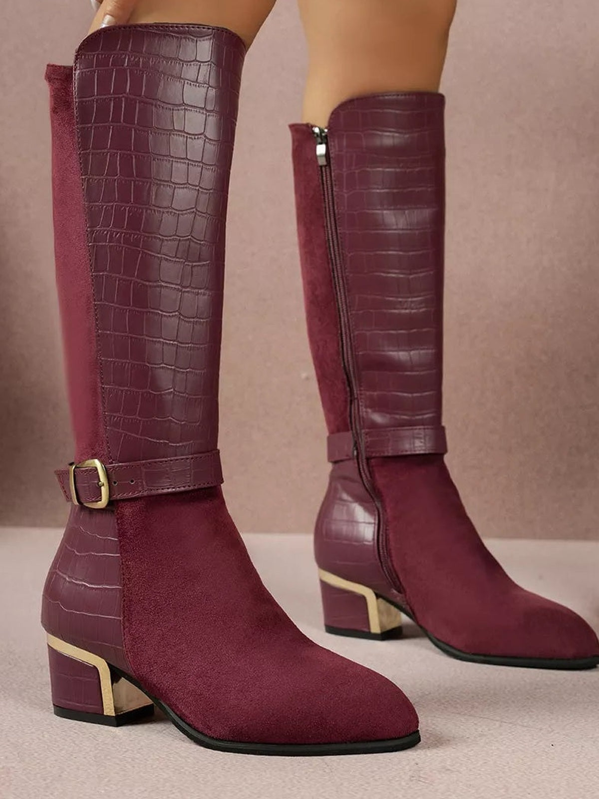 A model wears burgundy knee-high boots with crocodile-textured panels, suede fronts, side zippers, ankle buckles, and low block heels.