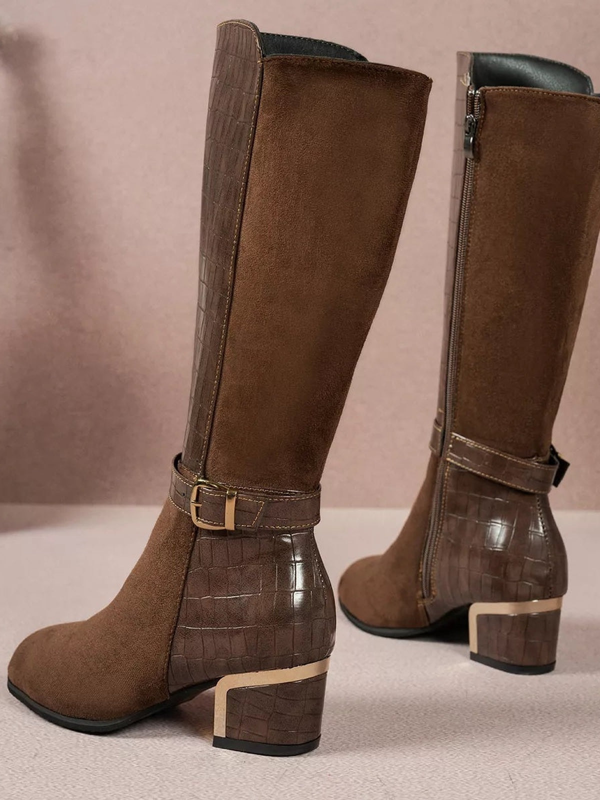 Brown crocodile-texture knee-high boots feature suede shafts and toes, low block heels, side zippers, and buckled ankle straps for a structured silhouette.