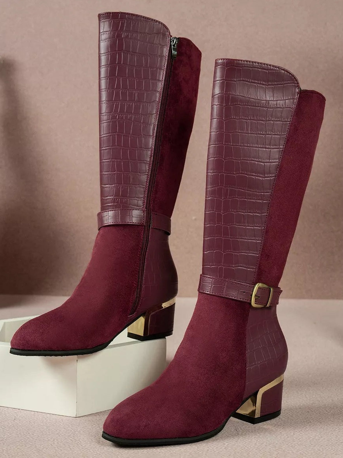 Burgundy knee-high boots feature crocodile-texture panels, soft suede-like shafts, side zippers, ankle straps with buckles, and low metallic block heels.