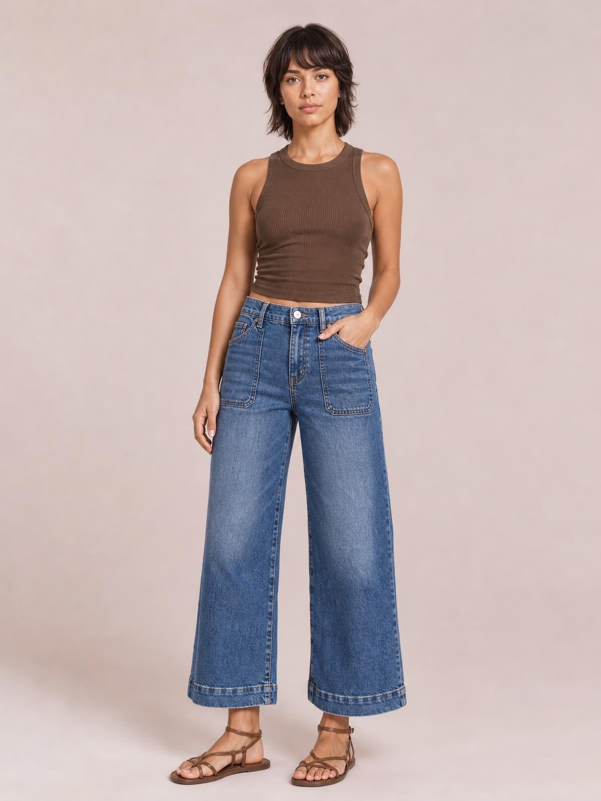 Model stands in medium-wash cropped high-rise wide-leg jeans with large front patch pockets, belt loops, and cuffed hems.