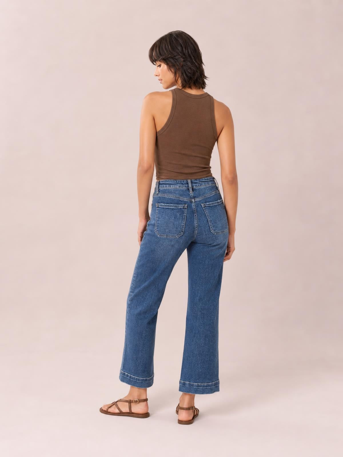 A model poses from behind in blue cropped high-rise wide-leg jeans with a structured waistband, belt loops, contrast stitching, and two back patch pockets.