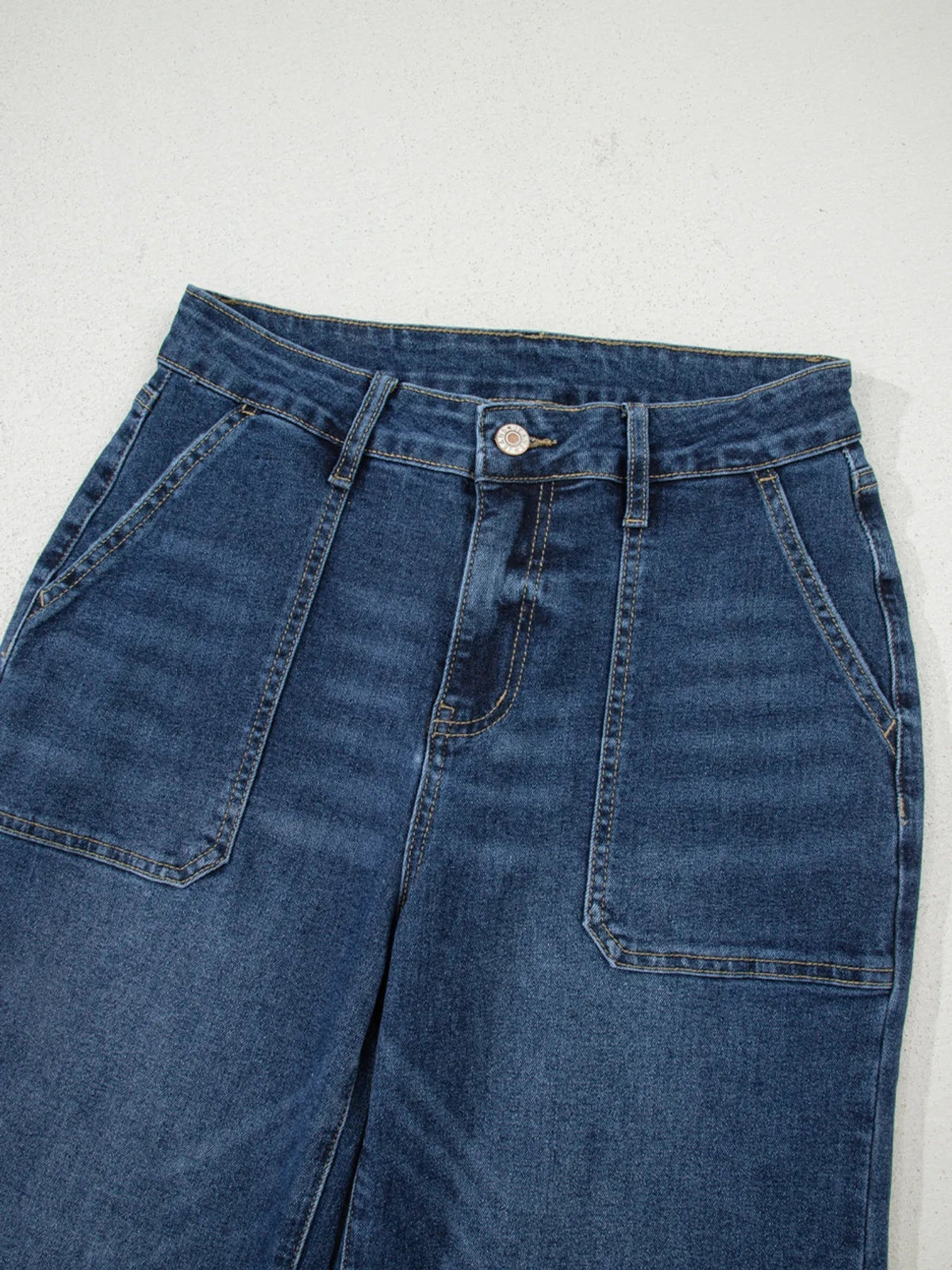 Dark blue high-rise wide-leg jeans shown close up with belt loops, a button fly, contrast stitching, and large front patch pockets.