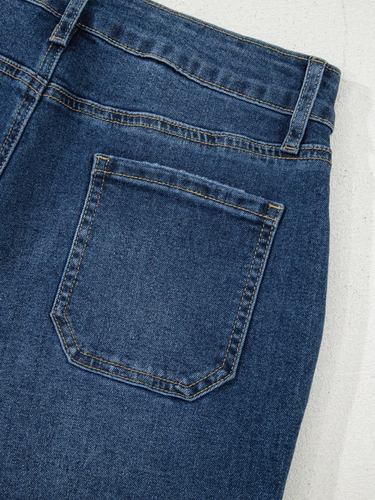 Close-up of dark blue cropped high rise wide leg jeans showing a back patch pocket, belt loop, and reinforced contrast stitching.