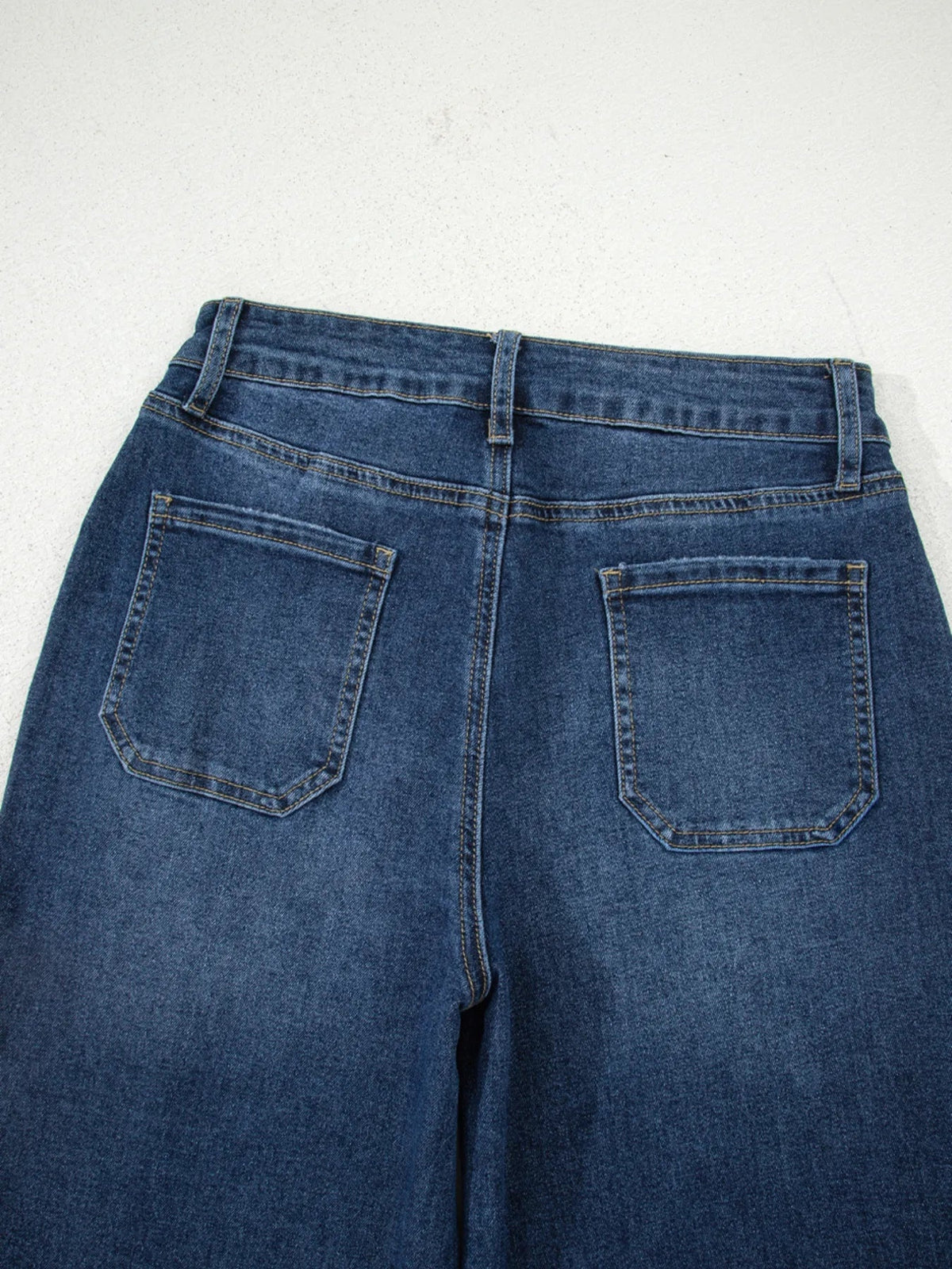 Close-up of dark blue cropped high-rise wide-leg jeans showing back pockets, belt loops, contrast stitching, and a structured denim construction.