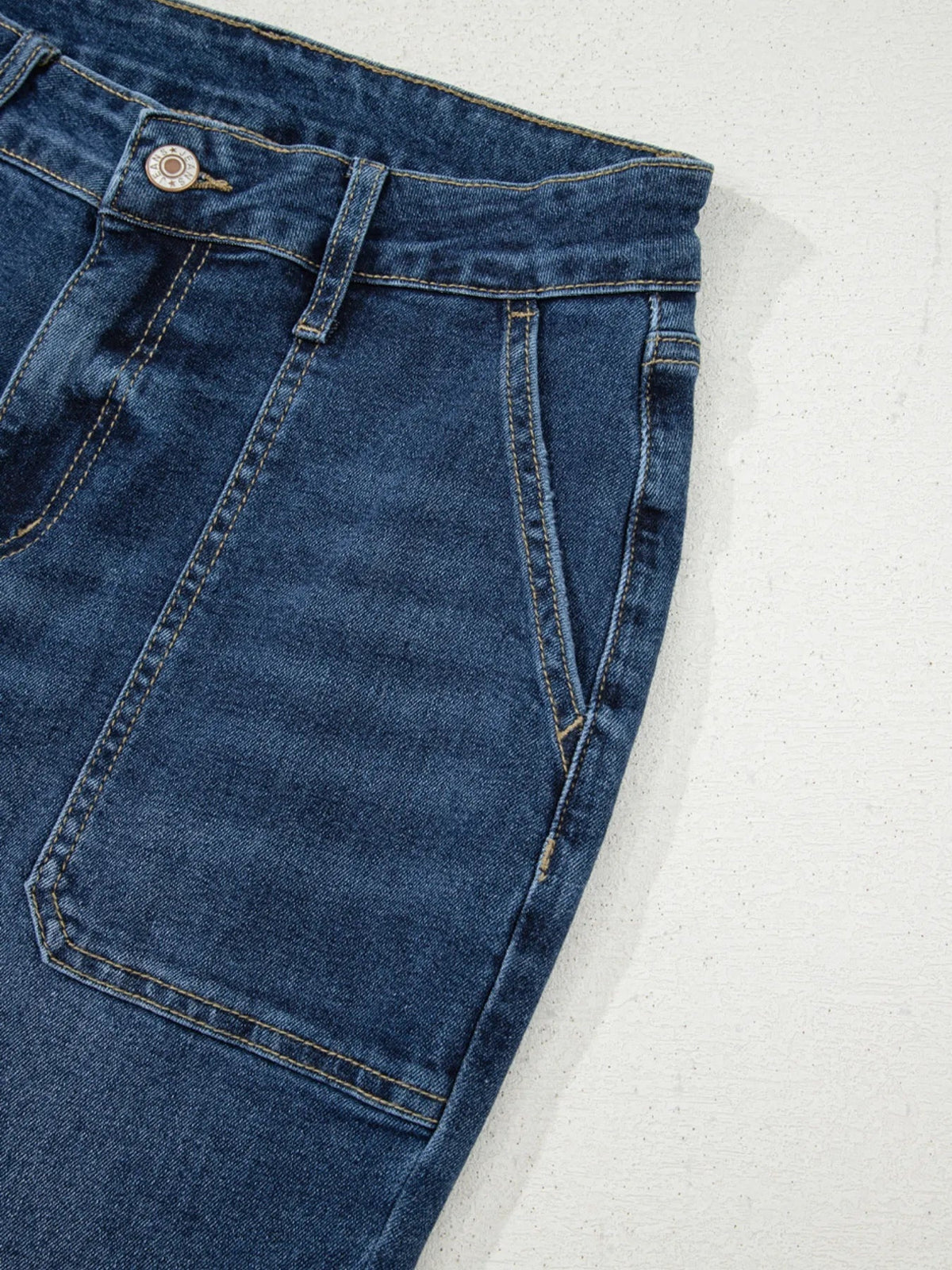 Dark blue cropped high rise wide leg jeans shown in close-up with a button waistband, belt loops, roomy pocket, and contrasting topstitching.