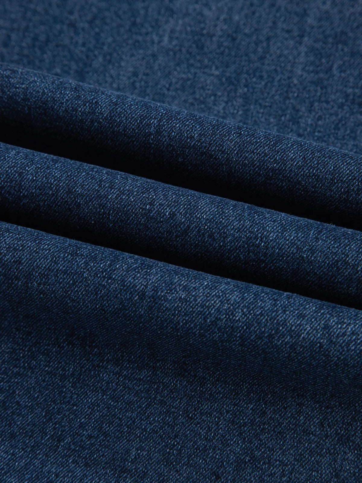 Close-up of dark blue denim fabric from cropped high rise wide leg jeans, showing its textured twill weave and structured folded construction.
