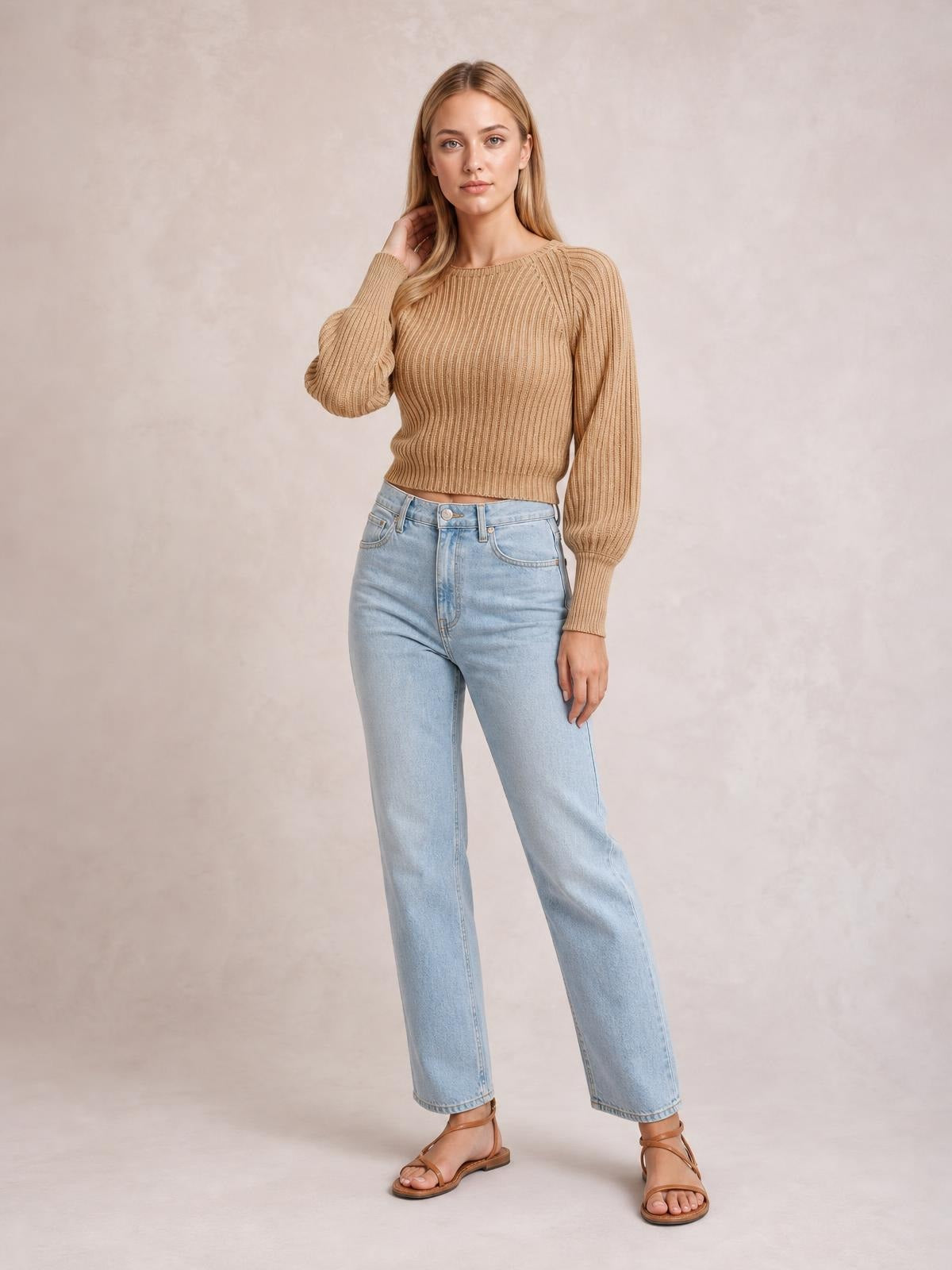 Model poses in a tan cropped round-neck ribbed pullover sweater with long raglan sleeves, fitted silhouette, and ribbed cuffs and hem.