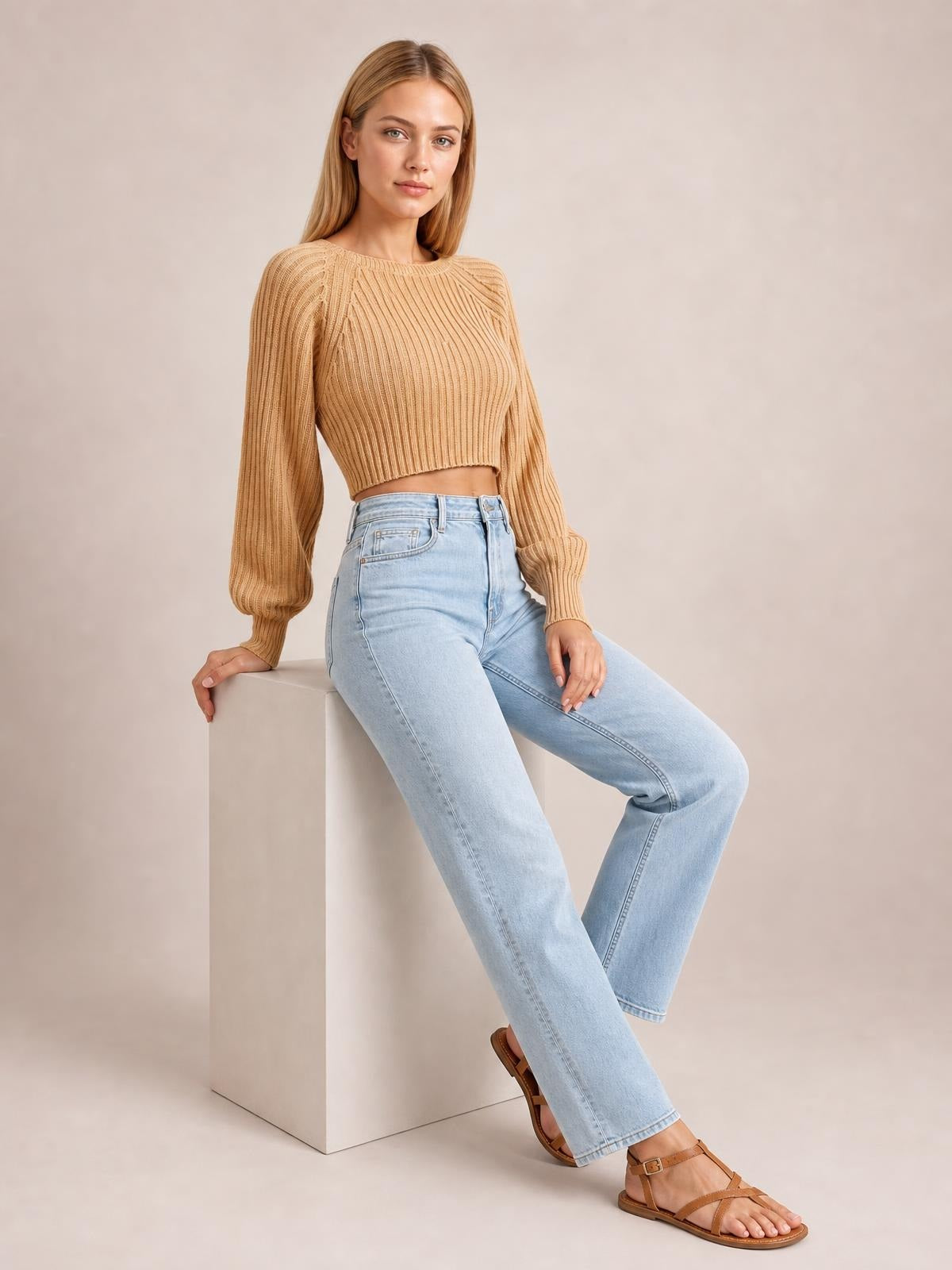 Model seated in a relaxed pose wears a camel cropped round-neck ribbed pullover sweater with long raglan sleeves and a fitted silhouette.
