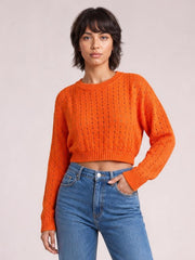 Model poses in an orange openwork round-neck sweater with long sleeves, ribbed cuffs and hem, and a cropped straight silhouette.