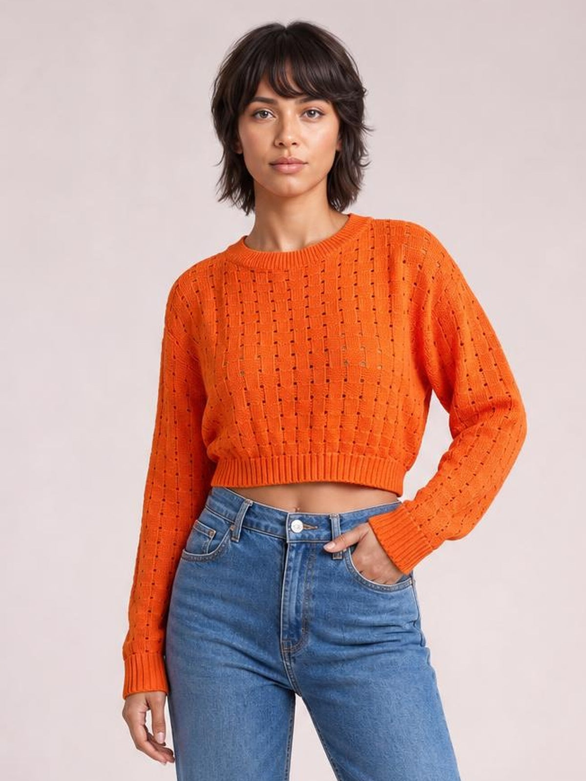 Model poses in an orange openwork round-neck sweater with long sleeves, ribbed cuffs and hem, and a cropped straight silhouette.