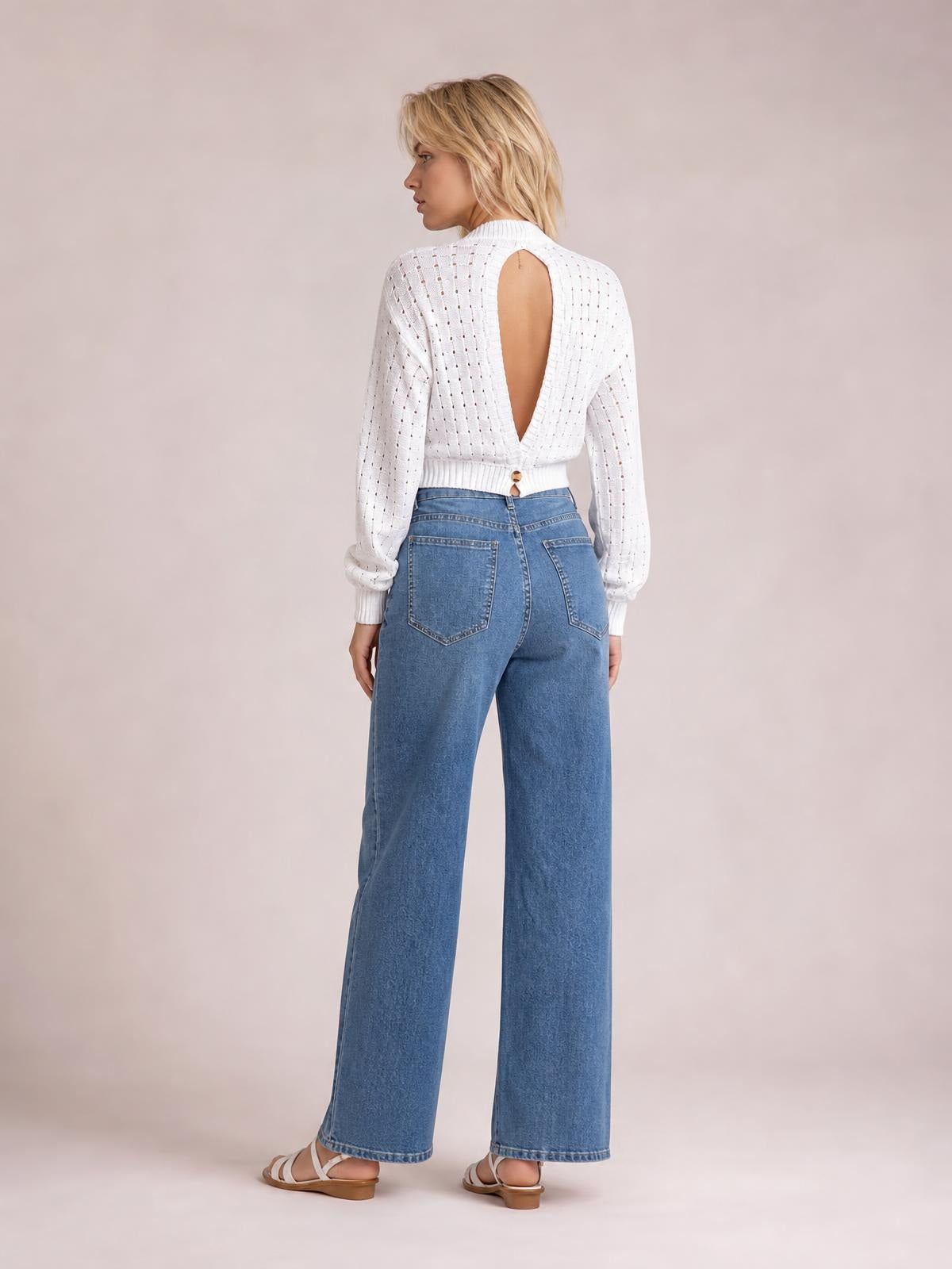 A model looks over her shoulder in a white openwork sweater with long sleeves, a round neck, ribbed trim, and a dramatic cutout back.