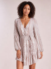 Model poses in a cream and brown striped surplice dress with long sleeves, a tied waist, relaxed silhouette, and ruffled tiered mini hem.