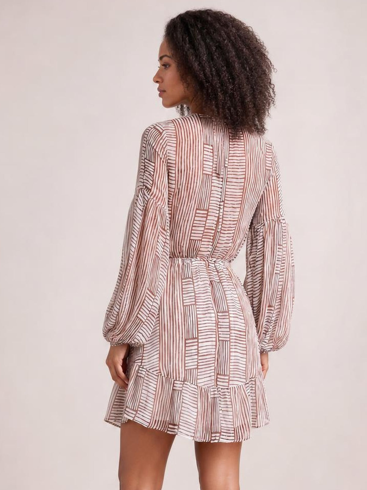 A model shows the back of a white and burgundy striped cutout dress with long puff sleeves, a tied waist, and a ruffled tiered hem.