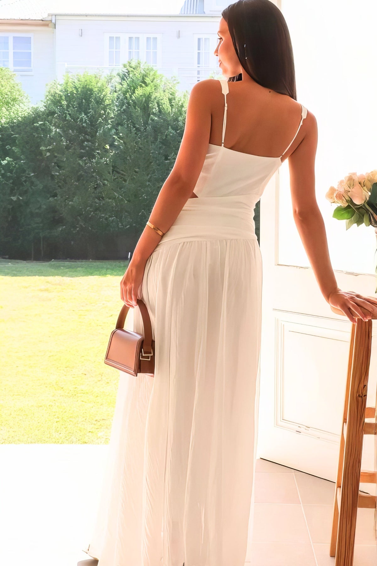 Model shown from the back in a cream Cutout Back V-Neck Dress with slim straps, a low cutout, ruched waist, and flowing floor-skimming skirt.
