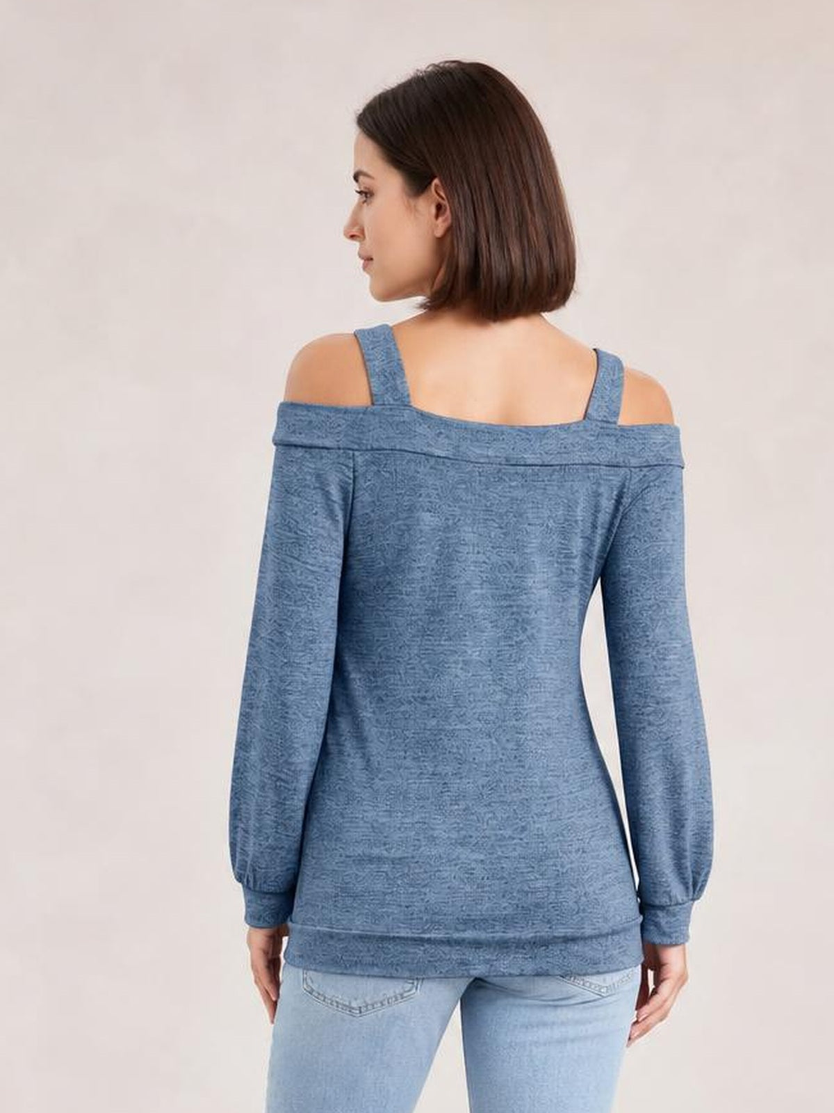 A model shown from behind wears a solid blue cutout cold-shoulder top with long sleeves, shoulder straps, a relaxed regular silhouette, and banded cuffs.