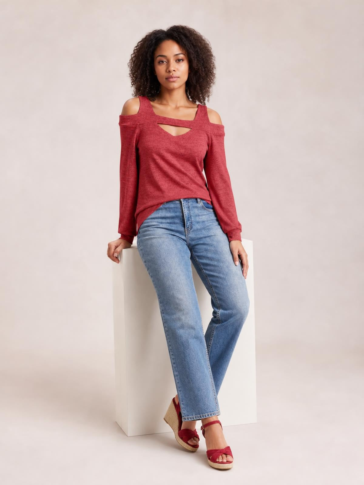 A seated model wears a solid red cutout cold-shoulder top with a square neckline, long sleeves, and a regular silhouette.