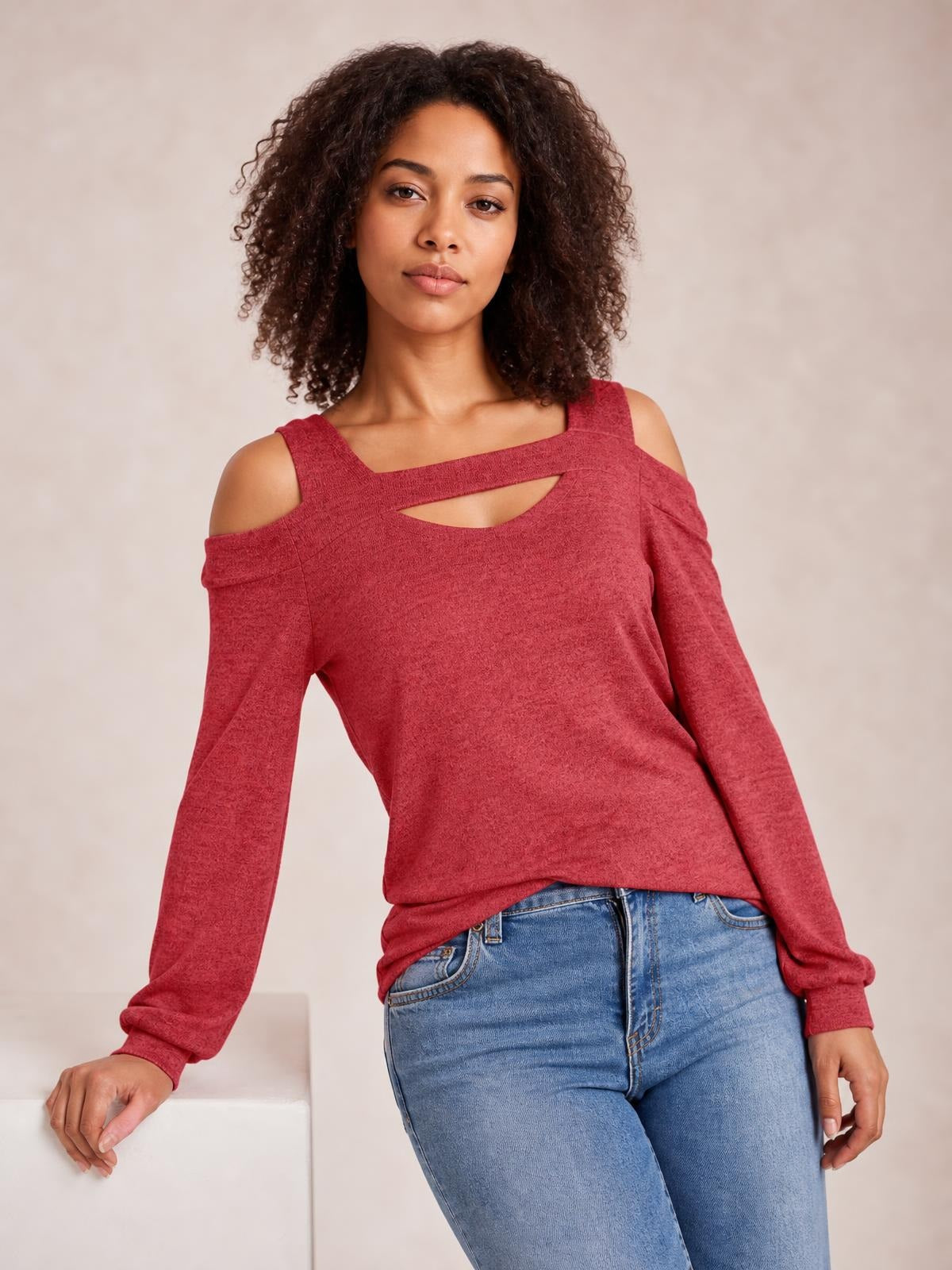 Model wears a solid red cold-shoulder top with long sleeves, square neckline, and a front cutout, shown in a relaxed leaning pose.