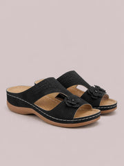 Black cutout flower open-toe flat sandals feature perforated crossover straps, layered floral embellishments, tan insoles, and contrast stitching on the rubber soles.