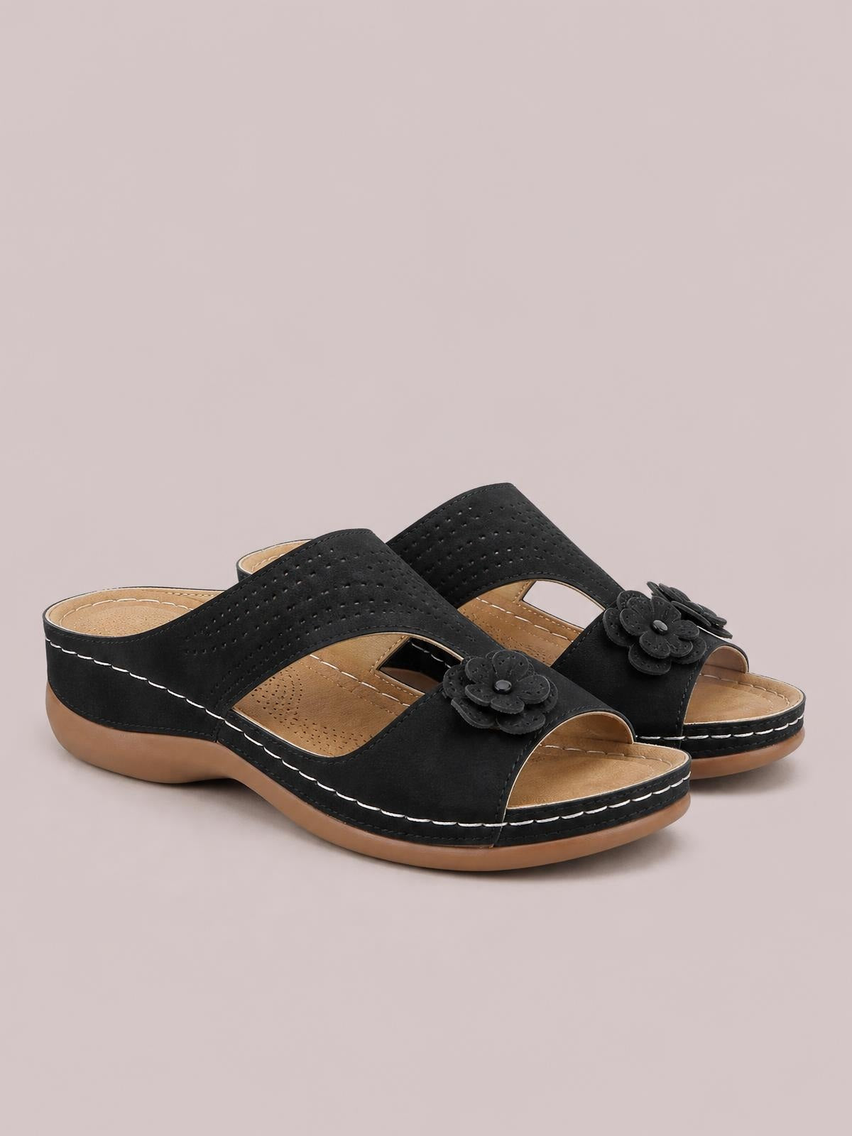 Black cutout flower open-toe flat sandals feature perforated crossover straps, layered floral embellishments, tan insoles, and contrast stitching on the rubber soles.