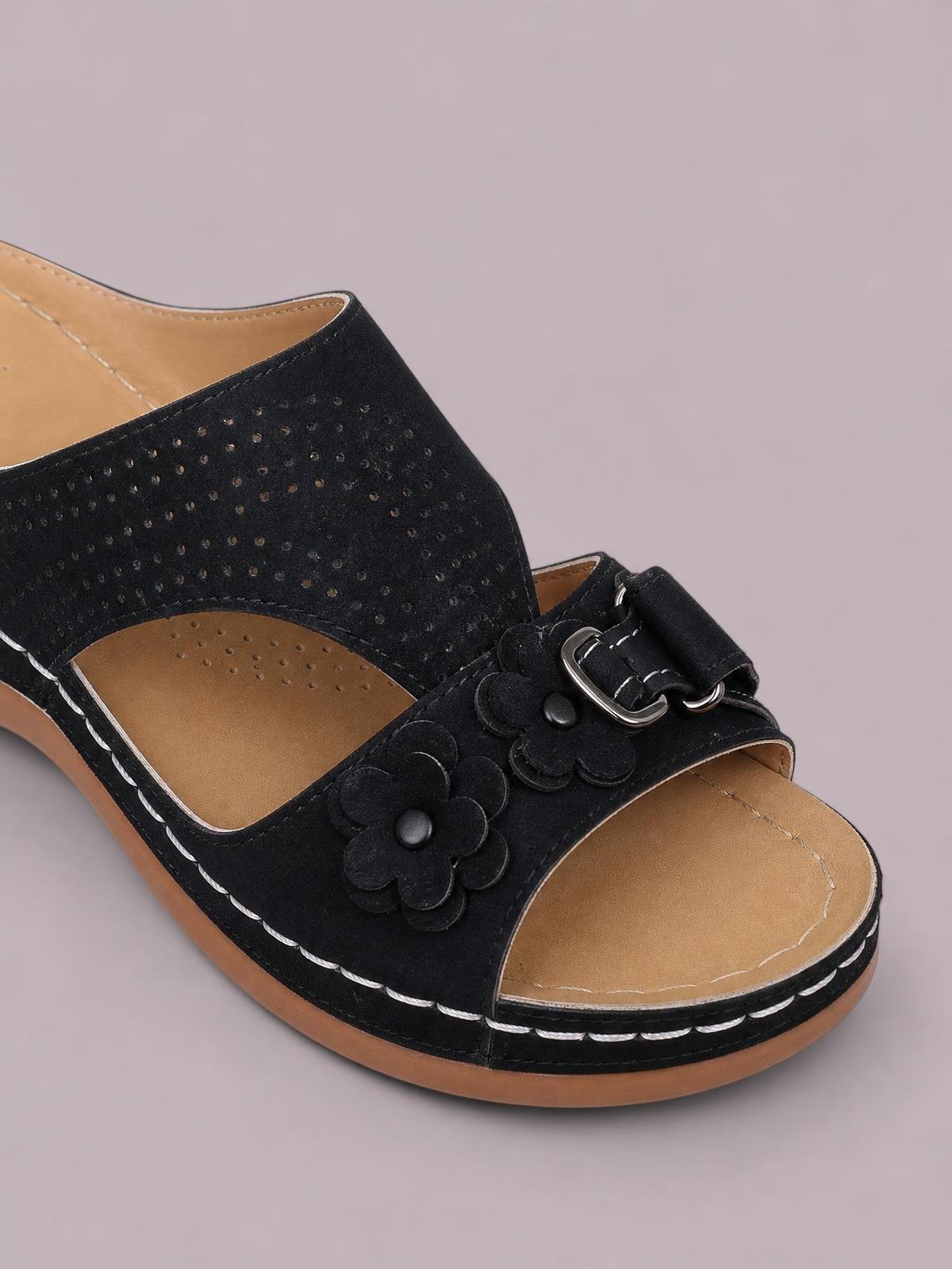 Black cutout flower open-toe flat sandals feature perforated uppers, layered floral appliqués, buckle straps, and contrasting white stitching.