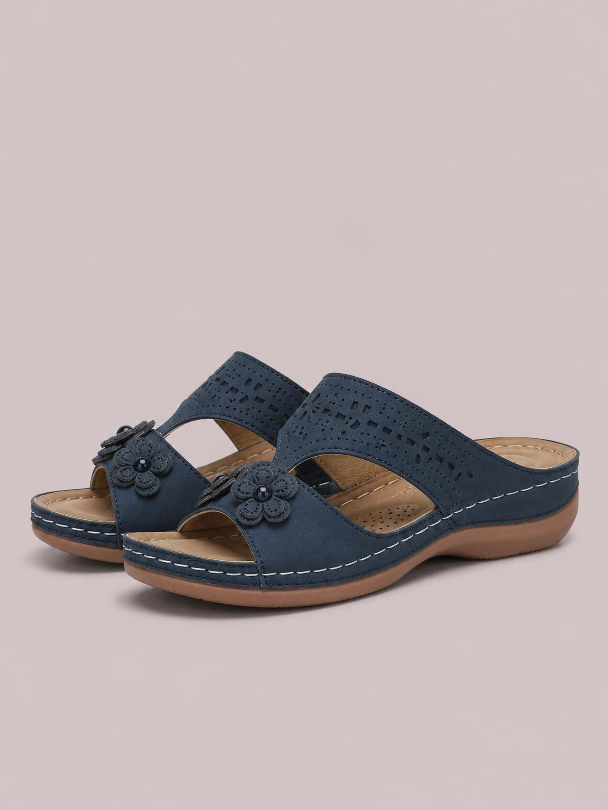 Navy blue cutout flower open-toe flat sandals feature perforated uppers, floral appliqué accents, cushioned insoles, and contrast stitching on rubber soles.