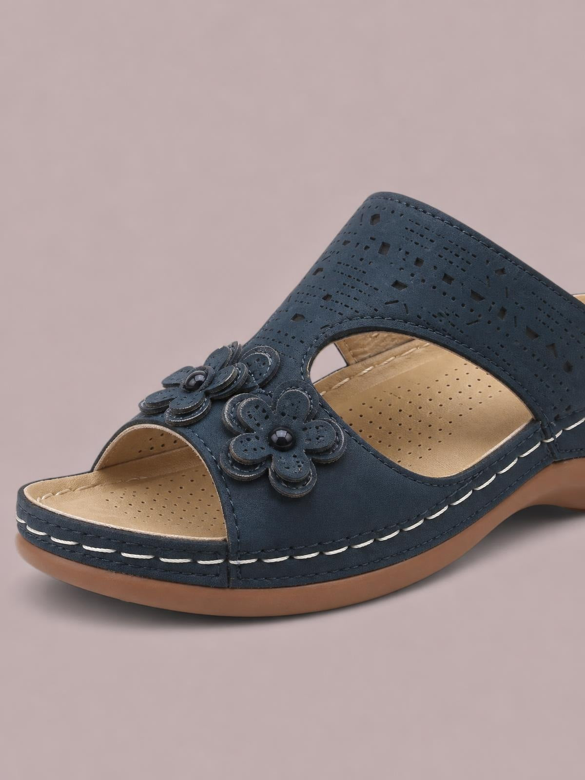 Navy cutout flower open-toe flat sandal with perforated upper, decorative floral appliqués, cushioned tan footbed, and contrasting stitched rubber sole.