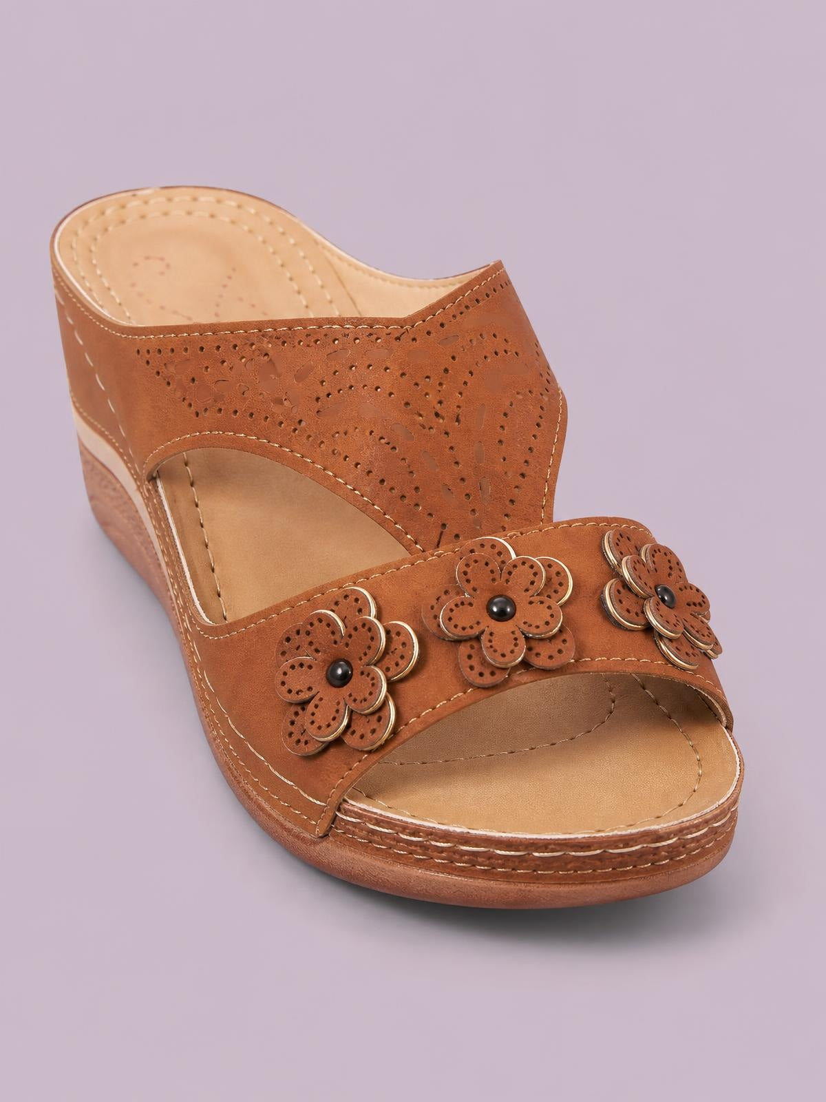 Brown open-toe flat sandals feature stitched PU leather straps with floral cutout embellishments and a layered rubber sole.
