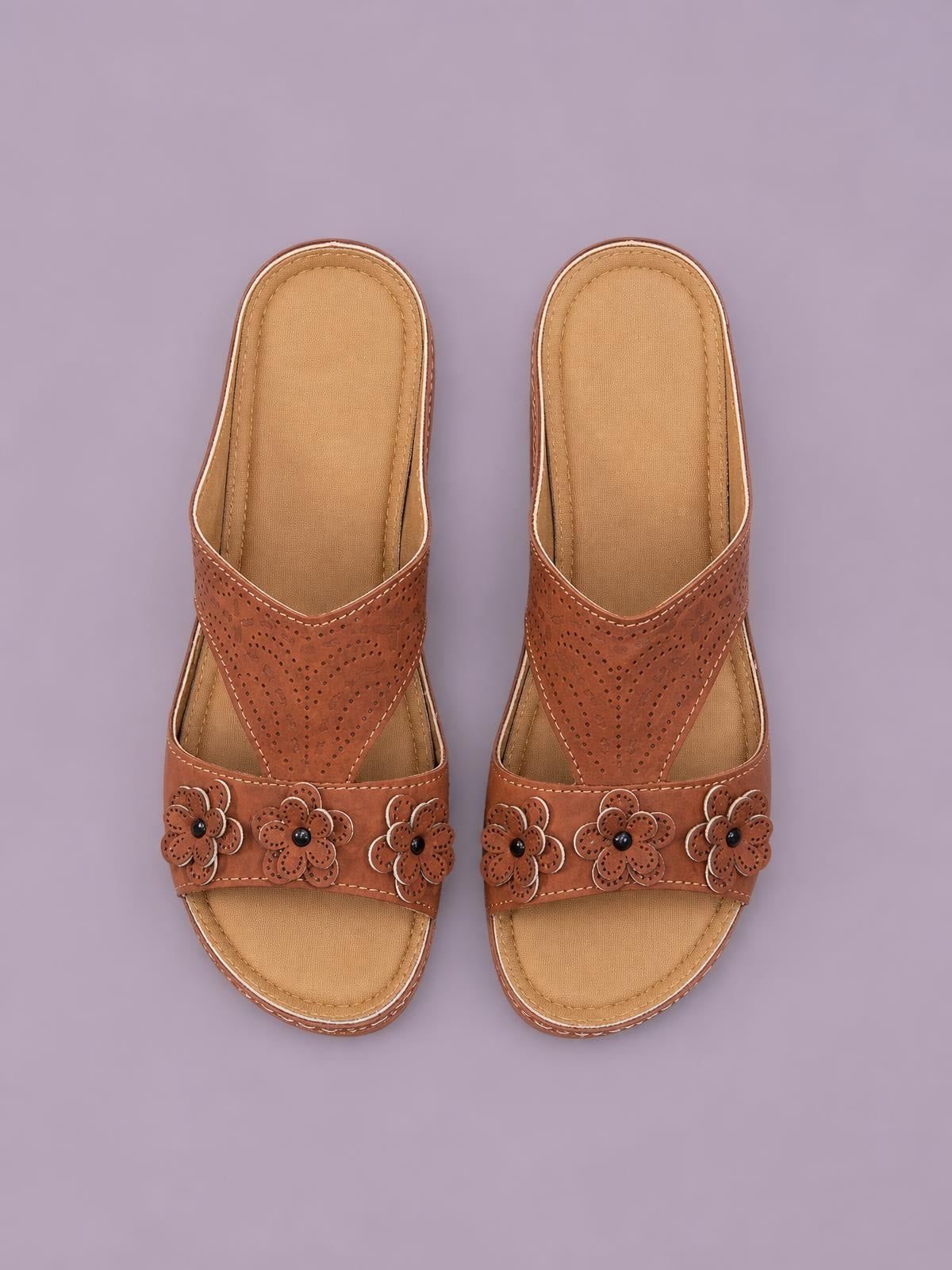 Brown cutout flower open-toe flat sandals feature perforated PU leather straps, floral embellishments, stitched edges, and cushioned tan footbeds.