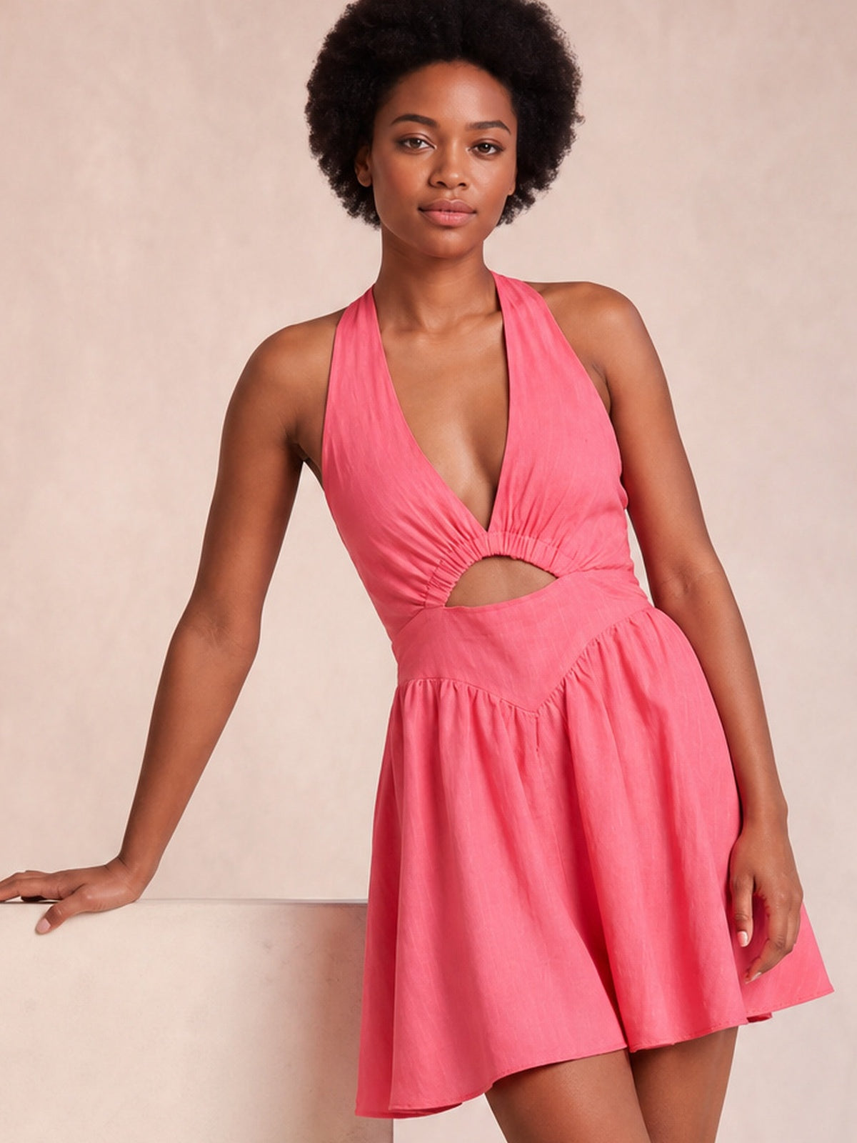 A model poses in a bright pink cutout halter neck mini dress with a ruched waist, deep neckline, and softly flared skirt.