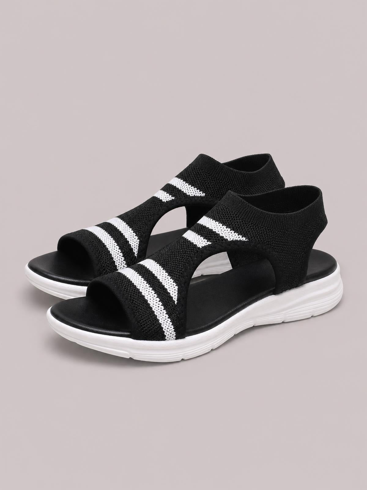 Black mesh cutout peep-toe sandals feature wide striped straps, open sides, and flat white textured soles.