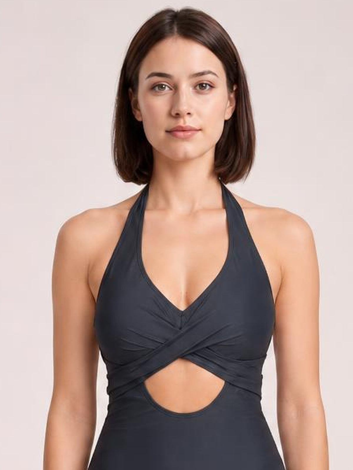 Front-facing model wears a dark halter-neck one-piece swimsuit with a deep V neckline, crossover ruching, and a prominent waist cutout.