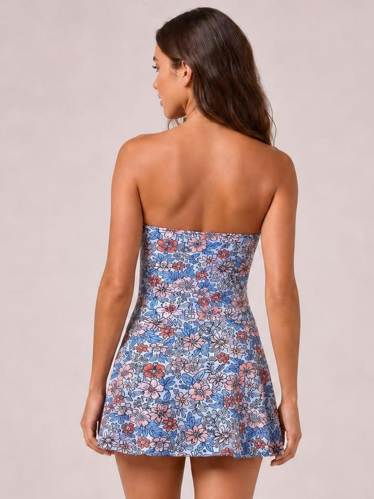 Back view of a model wearing a blue floral printed one-piece swimsuit with a fitted waist and flared skirted silhouette, holding the hem at both sides.