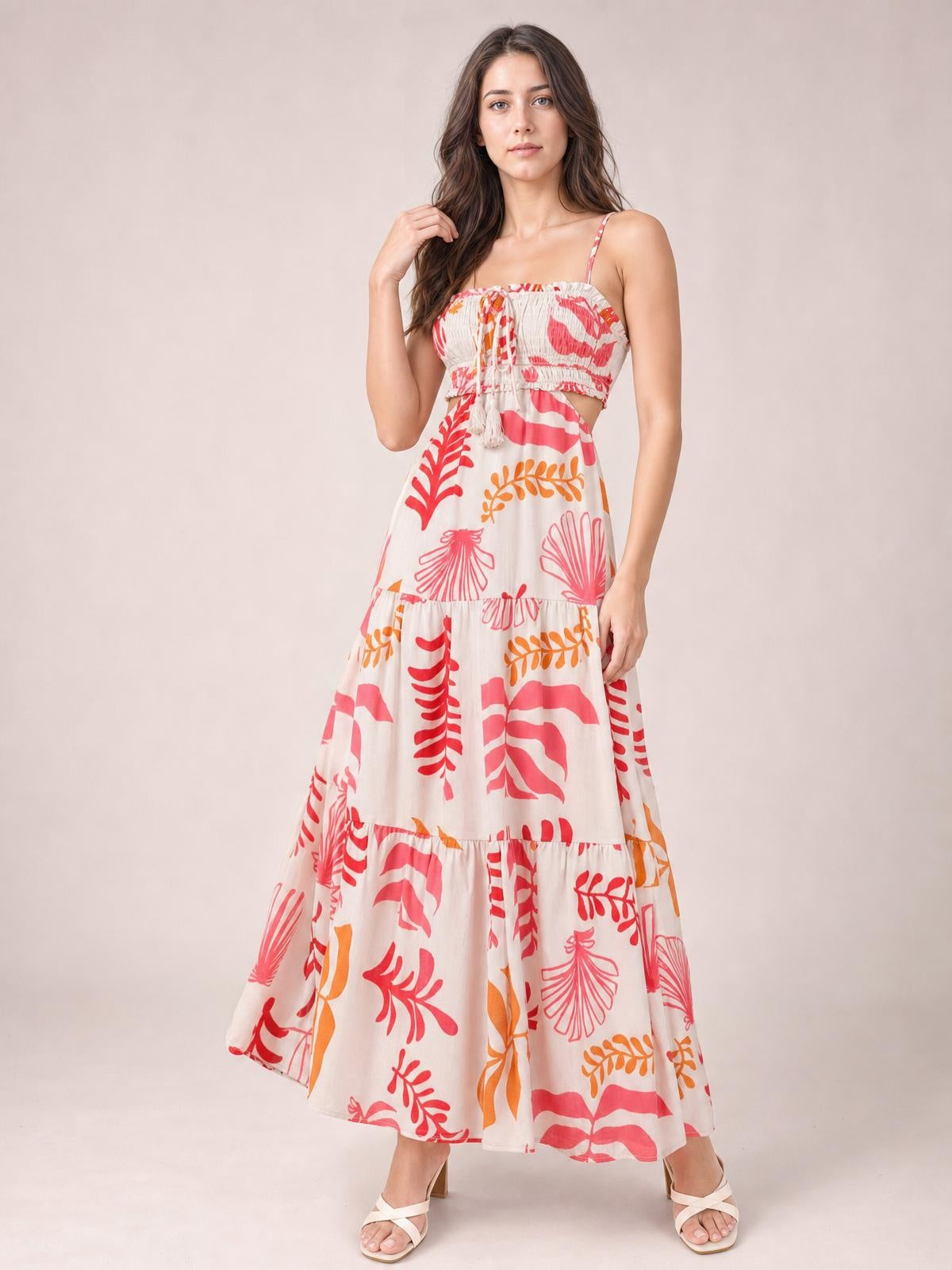 Model poses in a colorful printed sleeveless cami midi dress with thin straps, ruched smocked bodice, front tie, side cutout, and tiered skirt.