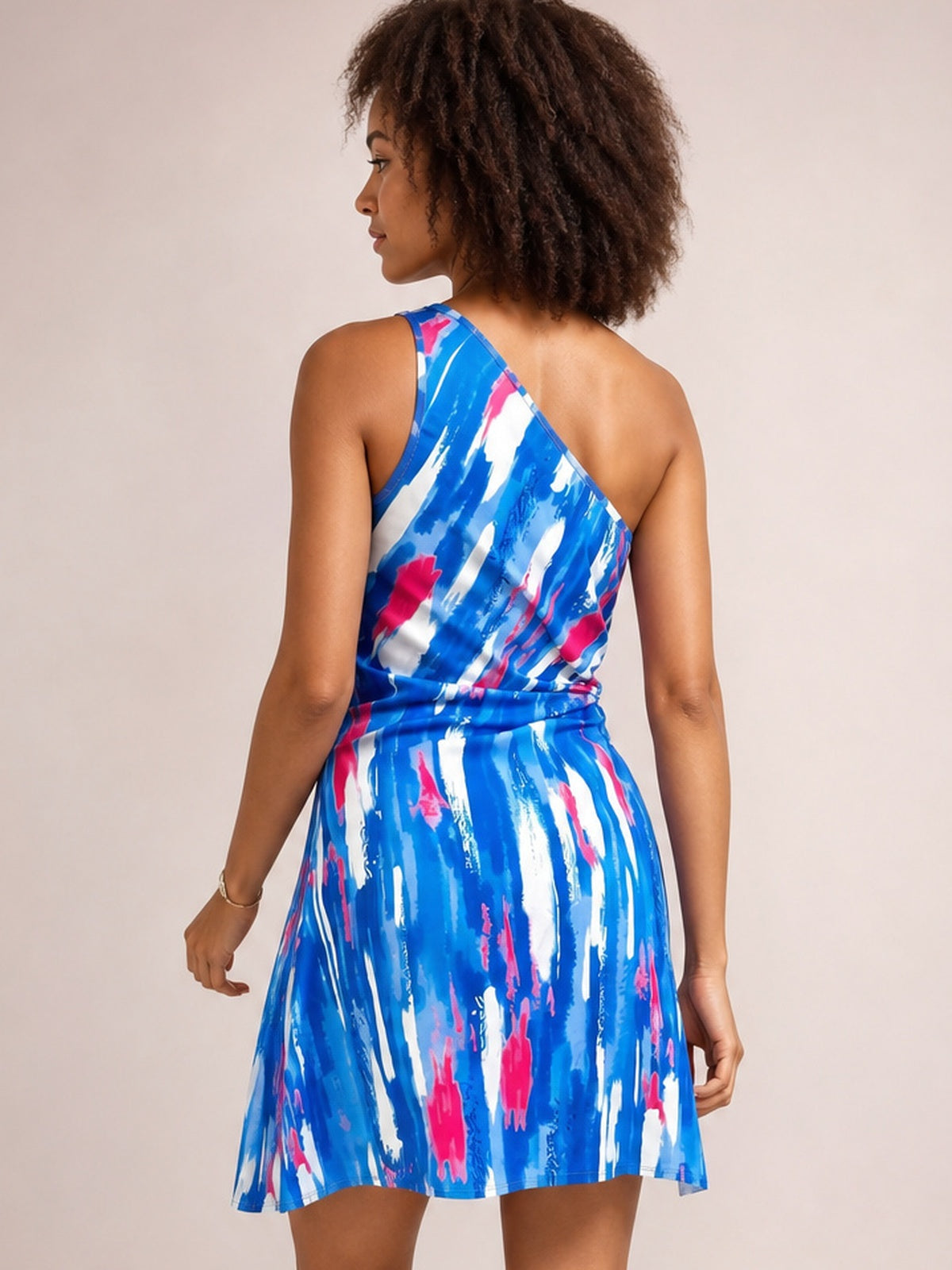 Model shown from behind in a blue and pink printed sleeveless mini dress with an asymmetric one-shoulder neckline, fitted waist, and softly flared skirt.