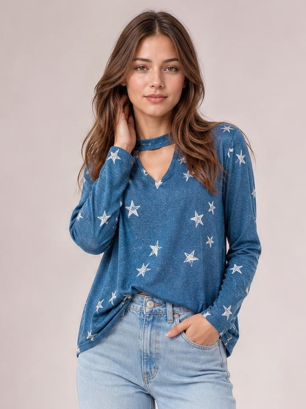 Model wears a blue star-print cutout round-neck long-sleeve T-shirt with a relaxed silhouette, visible neckline opening, and hand resting in a jeans pocket.