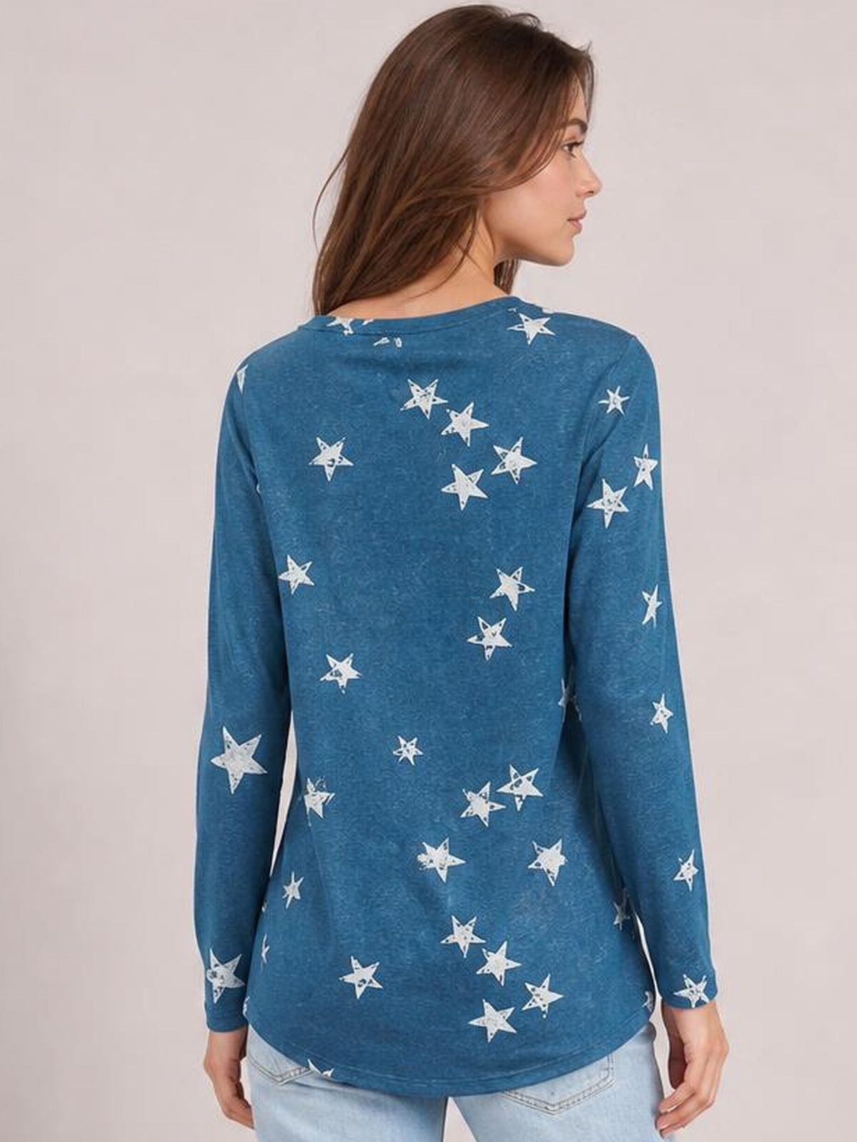 A model shown from the back wears a blue long-sleeve T-shirt with a round neck, scattered white star print, and relaxed straight silhouette.