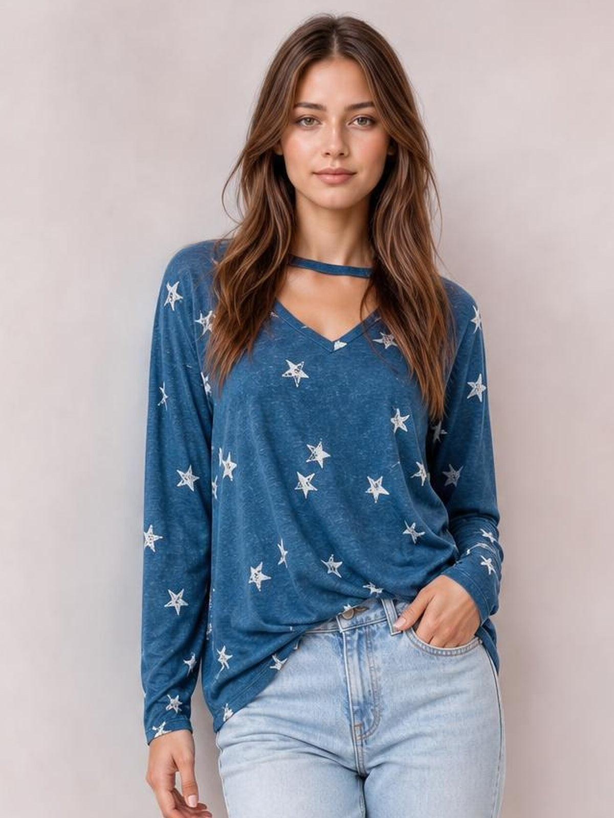 A model stands in a relaxed pose wearing a loose blue long-sleeve t-shirt with white star print and a round neckline featuring a chest cutout.